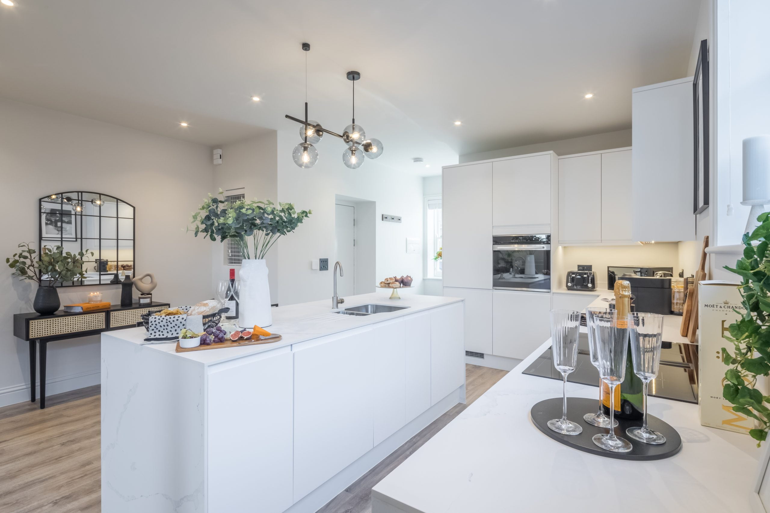 white modern kitchen with crittle mirror, hanging light fitting, kitchen island and champagne